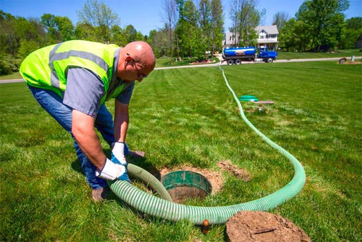 Septic tank treatment technician performing septic tank maintenance, with vacuum truck parked on the lawn